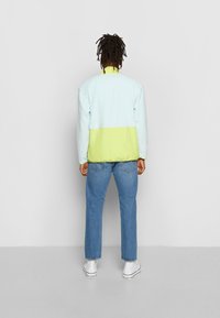 Giacca color bloc in blu chiaro e verde neon realizzata in tessuto morbido, con colletto alto e silhouette rilassata, abbinata a pantaloni in denim chiaro.