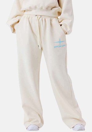 Pantalon de survêtement beige avec taille élastique et cordon de serrage, arborant un petit logo étoile bleu clair et le texte "pxp" sur la cuisse droite.