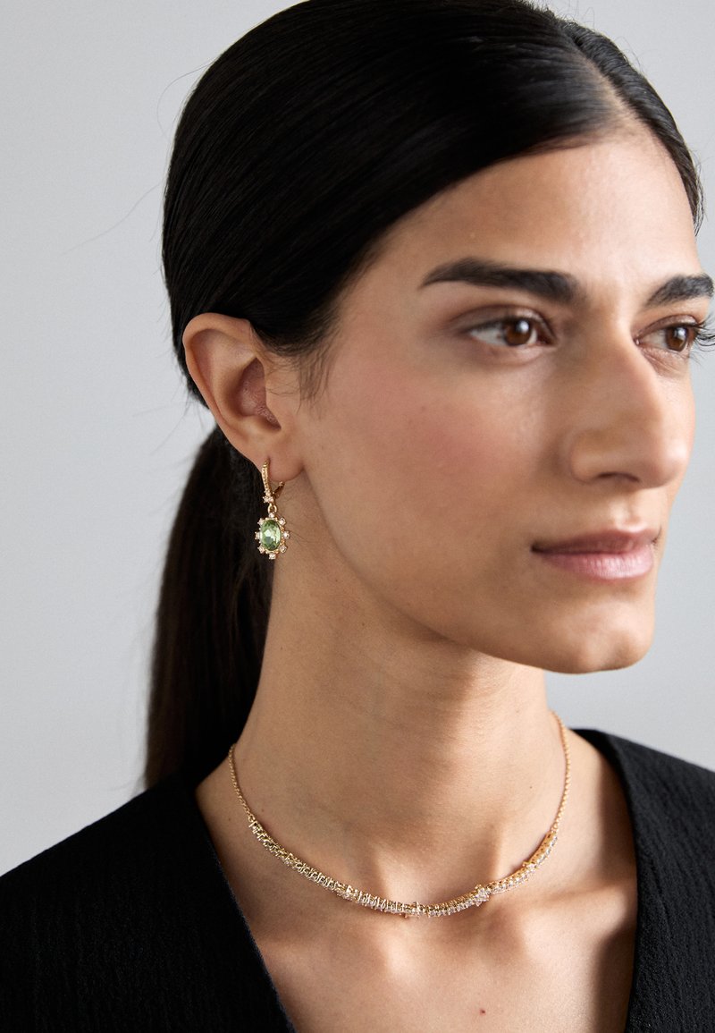 Goldschmuck mit einem grünen ovalen Stein, umgeben von kleinen klaren Steinen. Eine zarte Kette mit abwechselnden Gliedern unterstreicht das Design.