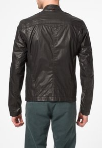 Svart läderjacka med smal passform, strukturerad yta och synliga stygn. Har en ståkrage och en ryggsjokdetalj.