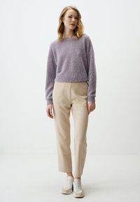Paarse donsachtige gebreide trui met lange mouwen, gecombineerd met hoog getailleerde beige pantalon en witte sneakers, tegen een effen achtergrond.