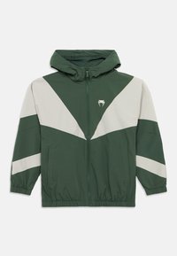 Πράσινο μπουφάν με ανοιχτό γκρι τριγωνικά μοτίβα, εμπρόσθιο φερμουάρ, κουκούλα και ελαστικά μανίκια. Διαθέτει πλαϊνές τσέπες και λογότυπο στο στήθος.