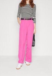 Rosa vida byxbyxor gjorda av ett slätt material, parat med en åtsittande svart-vitrandig topp. Accessoriserad med ett svart bälte och vita sneakers.