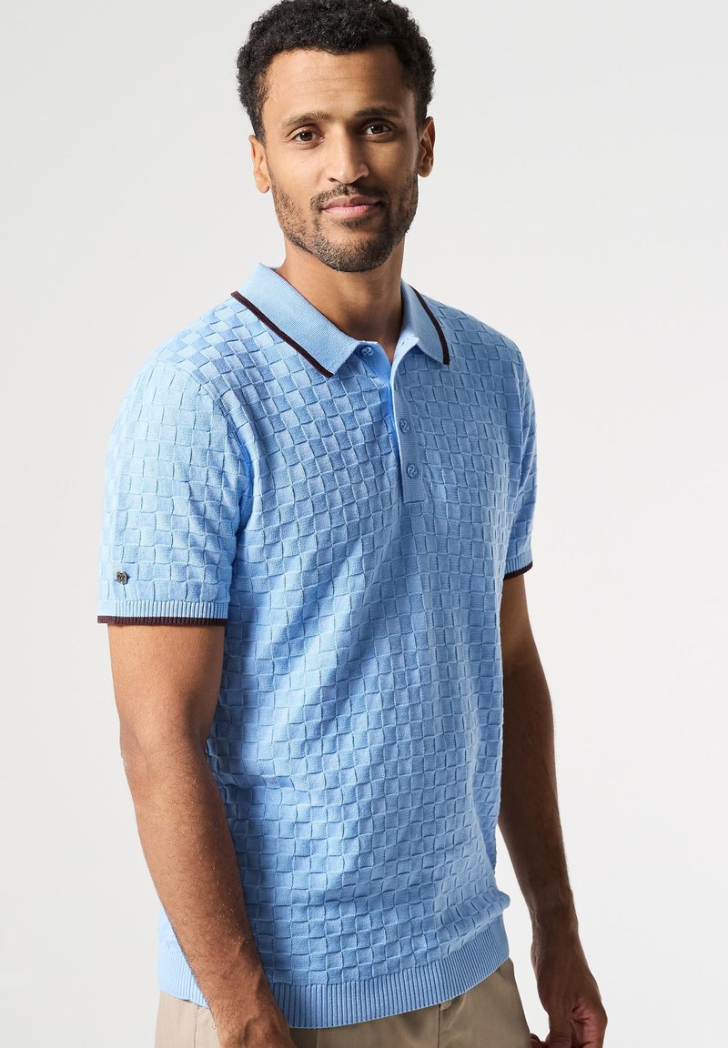 Světle modrá pletená polo košile s texturovaným čtvercovým vzorem, s kontrastním tmavým límcem a manžetami, předními knoflíky a žebrovaným lemem.