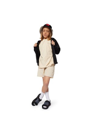 Enfant portant un short beige clair et un t-shirt, un sweat à capuche zippé noir, un chapeau seau noir, des chaussettes blanches et des sandales noires avec des sangles à motifs.