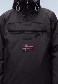 Anorak noir avec une poche zippée à l'avant, une capuche réglable avec des cordons blancs, et un patch drapeau norvégien sur la poitrine.