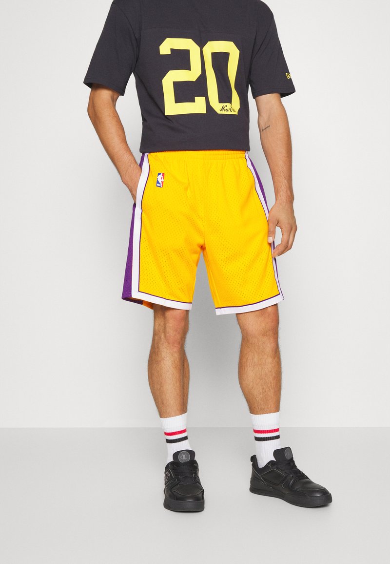 Pantaloni da basket gialli con accenti viola, strisce laterali e logo NBA. Abbinati a una maglietta nera con un grande numero 20 giallo.