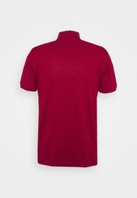 Punainen polo-paita, puuvillamateriaalia, lyhyet hihat, normaali kaulus, yksinkertainen muotoilu, ei näkyviä kuvioita tai yksityiskohtia. Takakuvasta.