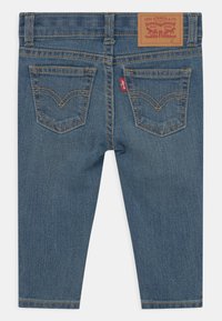 Jeans de mezclilla azul oscuro para niño con un diseño de pierna recta, que cuentan con dos bolsillos traseros, costuras doradas y un parche de logo de cuero marrón.