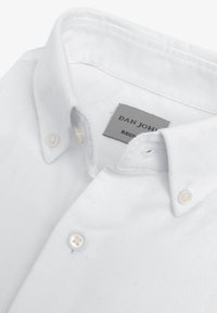 Camisa blanca de botón con un cuello estructurado, hecha de tela con cordones. Presenta una etiqueta con "DAN JOHN" y un cierre clásico con botones.