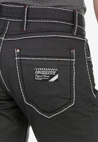 Zwarte denim jeans met contrasterende witte stiksels, een opvallend ontwerp van de achterzak en een merketiket op de achterkant.