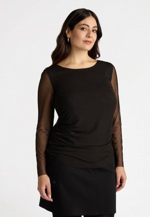 Zwarte top met een gladde, aansluitende pasvorm en doorschijnende lange mouwen; ronde halslijn. Model gecombineerd met een zwarte rok en zwarte leggings.