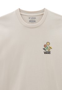Camiseta de algodón beige con cuello redondo, que presenta un pequeño gráfico floral multicolor y el logo "VANS" en la zona del pecho. Corte clásico.