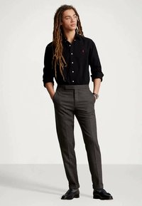 Sort skjorte med knapper, grå bukser med mønster og svarte dressko. Skjorten har en liten logo, og buksene har en skreddersydd passform.