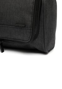 Grå tygväska med texturerad yta, featuring en svart dragkedja, liten lapplabel och en elegant rektangulär design.