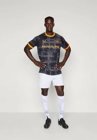 Crni nogometni dres s sivo-smeškanim uzorcima, narančastim ovratnikom i logom, uparen s bijelim šortsem i čarapama, te crnim kopačkama.