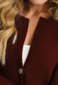 Donna bionda che indossa un cardigan a maglia bordeaux con colletto a coste e un solo bottone sopra un top bianco a coste.