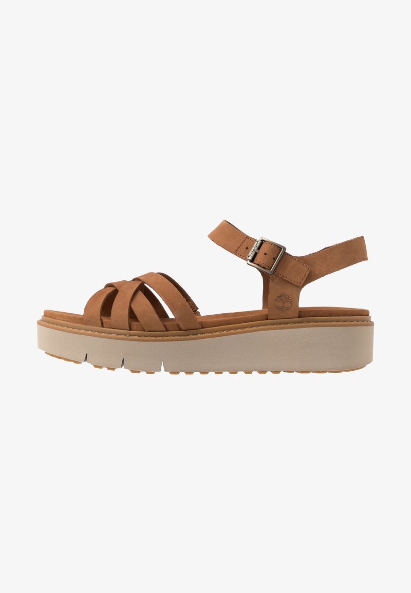 Sandale en cuir marron avec brides croisées, boucle réglable et semelle blanche épaisse avec dessous cranté.