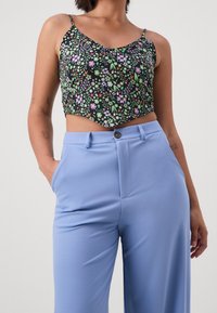 Avskuren svart topp med färgglad blommönster, i kombination med ljusblå högmidjade byxor med framknäppning och slät textur.