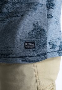 Krátký rukáv v námořnické modré barvě s texturovaným vzorem, s logem našitým na lemu a pruhovanými akcenty u výstřihu.