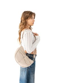 Borsa a tracolla beige con una morbida texture a trapunta, dotata di una tasca con zip e una tracolla regolabile. Indossata da una persona su uno sfondo bianco.