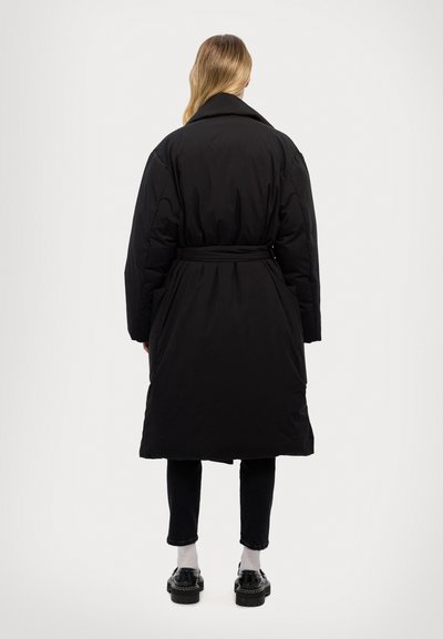 Black padded coat with a belt, large collar, and long sleeves. The back shows a smooth texture and knee-length design, paired with black pants.