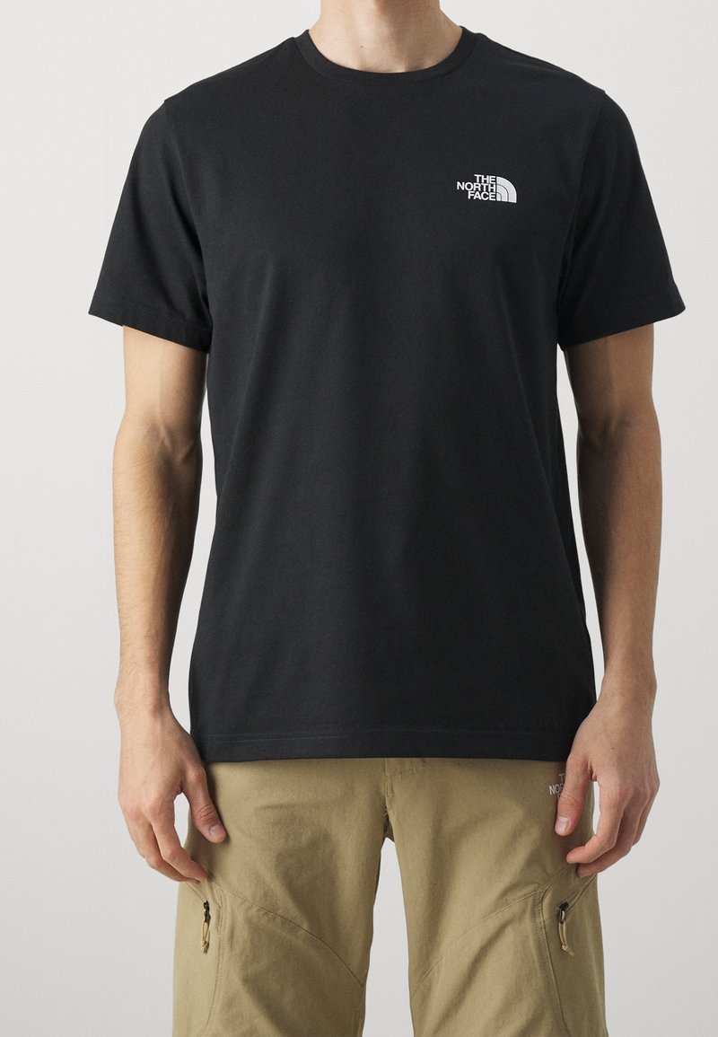 Černé tričko s krátkým rukávem a malým bílým logem The North Face na levé části hrudi, nošené s béžovými cargo kalhotami se zipovými kapsami.