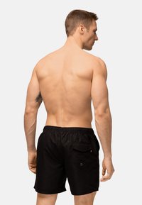 Pantaloni da bagno neri realizzati in materiale leggero, con vita elastica e una tasca posteriore con un piccolo accento decorativo.