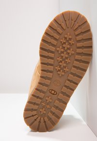 Suela de bota de goma marrón con un patrón de banda de rodadura profundo. Las características incluyen surcos hexagonales y en forma de estrella para mejorar la tracción y una impresión de logotipo.