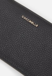 Portafoglio in pelle nera con texture, caratterizzato da logo in rilievo dorato. Forma rettangolare con chiusura a cerniera e dettagli di cucitura discreti.