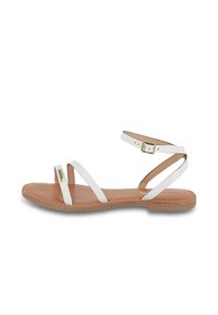 Sandali piatti bianchi in pelle con tre cinturini stretti, fibbia regolabile alla caviglia e soletta color tabacco. Dettagli di cucitura notevoli lungo la suola.