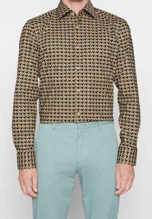 Button-up shirt with a houndstooth pattern in brown and black, featuring a classic collar and long sleeves. Paired with light blue trousers.
