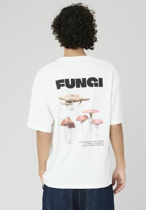 T-shirt en coton blanc avec un graphique de divers champignons et le mot "FUNGI" en lettres noires en gras au dos. Manches courtes, coupe décontractée.