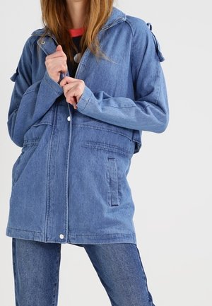 Woman wearing a blue denim jacket with front pockets, button and zipper closure, paired with blue jeans.