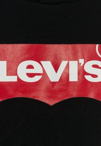 Sudadera negra con un destacado logotipo rojo que tiene un borde inferior curvado y texto blanco que dice "Levi's". Textura suave, diseño sencillo.