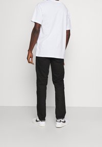 Camiseta de algodón blanca de manga corta, combinada con pantalones negros y zapatillas blancas con acentos negros y suela texturizada.
