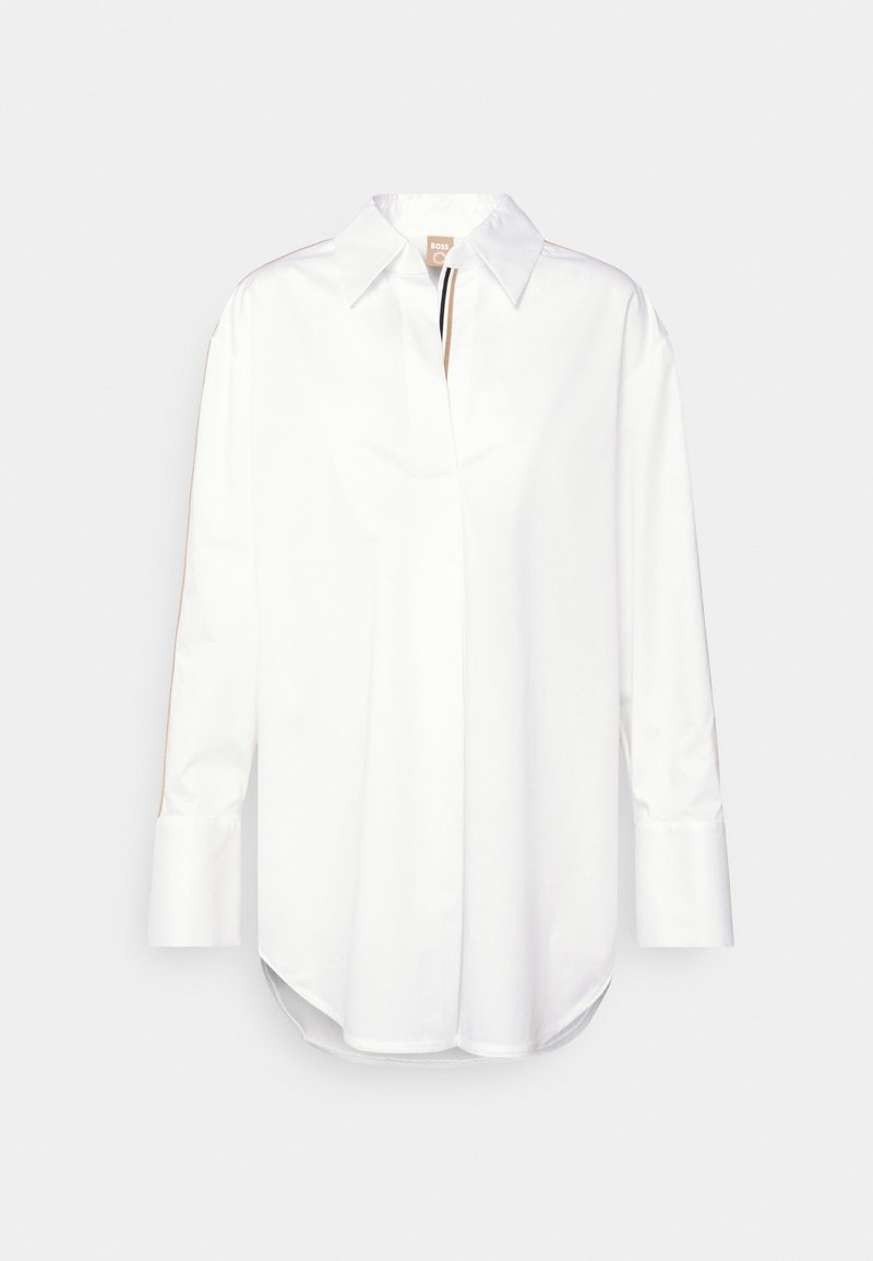 Vit långärmad skjorta med knappar och spetsig krage, samt bruna och svarta detaljer längs insidan av knäppningen och ärmarna.