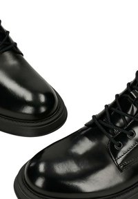Scarpe in pelle nera con finitura lucida, punta rotonda e design con lacci. Caratterizzate da una suola in gomma testurizzata e cuciture visibili.