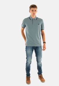 Polo shirt di colore azzurro chiaro con colletto e polsini a righe nere, abbinato a jeans in denim blu e stivali color sabbia, che presenta un look casual.