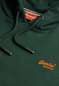 Groene katoenen hoodie met verstelbare trekkoorden en oranje "SuperDry" logo. Heeft een geribbelde halslijn en een gestructureerde stofafwerking.