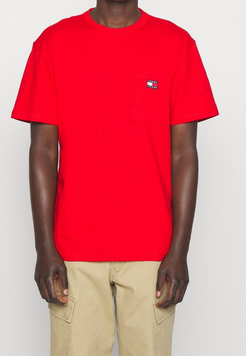 Rød bomulds t-shirt med korte ærmer, rund halsudskæring og en lomme på brystet, der har et lille mærke logo. Glat tekstur.