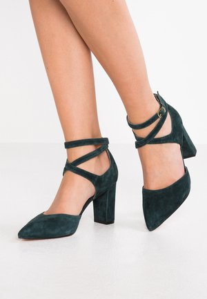 Chaussures à talons hauts en daim vert foncé avec un design à bout pointu et des lanières croisées autour de la cheville ; surface texturée ; talon épais.