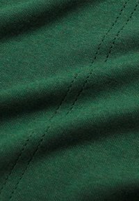 Nahaufnahme von grünem Stoff mit sichtbarer Naht und subtiler Textur, die feines Strickmuster und sanfte Falten zeigt.