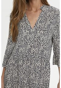 Šaty s květinovým vzorem, které mají V-výstřih, tříčtvrteční rukávy a nařasený pas v odstínech námořnické modři a krémové.