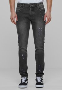 Mustad denim püksid sale lõikega, kulumise detailidega ja valgete värvilaikude aktsentidega. Viimistletud viie tasku ja nupuga sulgemisega.