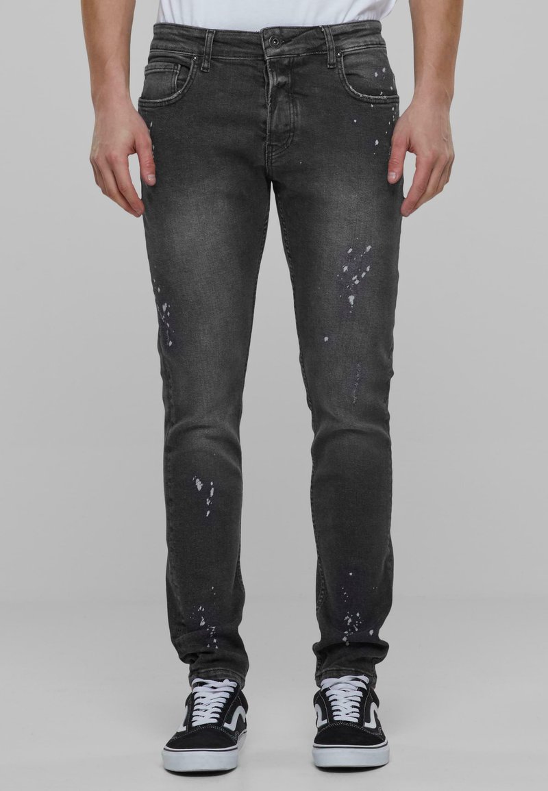 Jeans de mezclilla negros con corte ajustado, detalles desgastados y salpicaduras de pintura blanca. Terminados con cinco bolsillos y cierre de botones.