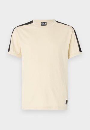 Short-sleeve, beige t-shirt made of cotton. Features black accents on shoulders and a small logo tag on the bottom left.