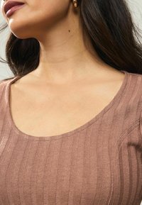 Haut en tricot côtelé marron avec un large décolleté, présentant une texture lisse et un subtil brillant, soulignant la forme du décolleté.