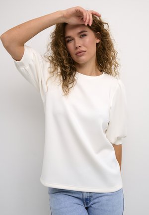 White, short-sleeve top in a soft material with a relaxed fit, featuring a round neckline and slightly puffed sleeves, paired with blue jeans.