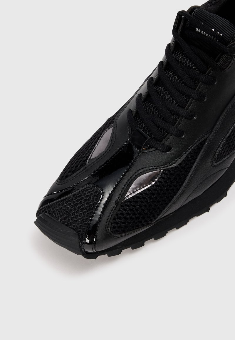 Zwarte sportieve schoen met een bovenwerk van mesh, glanzende accenten en een textuurrubber zool. Inclusief vetersluiting en kenmerkende zijpanelen.